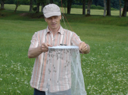 Dr. Berg hält auf einer Wiese das Fangnetz mit Drohnen in den Händen