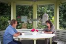 Frau und Man in einer Gartenlaube gegenüber am Tisch sitzend 
