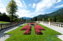 Blick über Terrasse mit Blumenrabatten auf die  Alpen