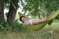 Frau in einer grünen Hänmgematte unter Bäumen liegend