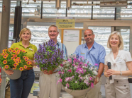Drei Gewinner mit ihren eigenen Blumen in der Hand haltend, daneben die Organisatorin mit dem Mikrofon