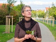Dr. Susanne Böll mit Blättern in der Hand neben einem Baum.