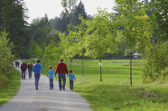 Einige Erwachsene und Kinder gehen auf einem Weg am Waldrand spazieren.