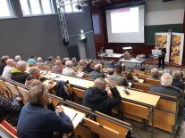 Personen sitzen in Sitzreiehen und schauen nach vorne zur Vortragenden in der Aula der LWG.