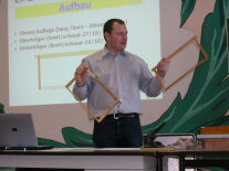 Ein Referent zeigt Holzrähmchen für die Imkerei in einem Lehrsaal.
