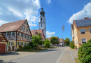 Schmale Vorgärten mit Rasen, Sträuchern und Bäumen begleiten die Straße im Dorf