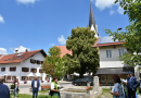 Ein Dorfplatz mit einem großen Brunnen, im Hintergrund ein großer Lindenbaum und die Kirche.