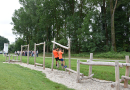 Kinder auf einem Spielplatz mit einem Gerät aus runden Holzbalken zum Klettern und Balancieren.