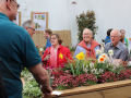 Besucher stehen an einem mit Blumen und Kräutern bepflanzten Hochbeet aus Holz.