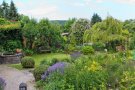 Blick über einen Garten mit Staudenbeeten, Rasenflächen, Brunnen und Bäumen