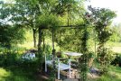 Sitzplatz unter Gartenpavillon mit weißem Tisch, weißer Bank und Holzstühlen