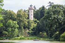 Blick über einen See auf eine von Bäumen umsäumten Turm