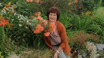 Frau mit orangefarbener Jacke auf einer Mauer sitzend daneben gleichfarbige Rosen Taglilien