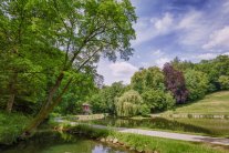 Weiher umgeben von Baumbestand und hügeligen Wiesen