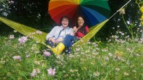 Zwei Frauen in einer Hängematte unter einem Regenschirm in Regenbogenfarben sitzend.