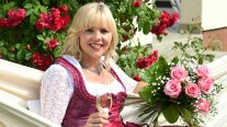 Frau mit Dirndl, Rosenstrauß und Sektglas in einer Hängematte sitzend