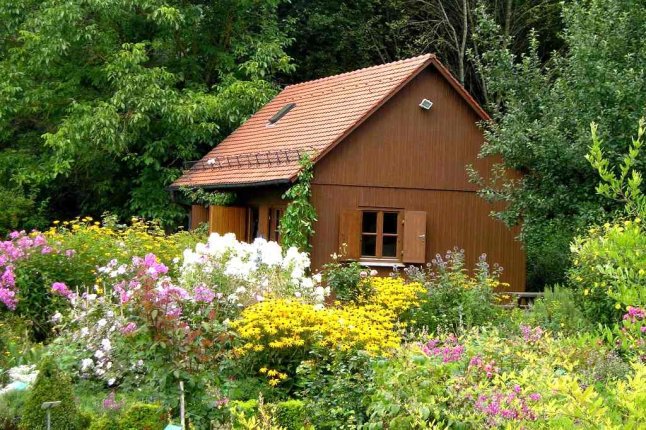 Blick über Staudenbeete in sommerlichen Farben auf ein Holzgartenhäuschen