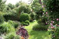 Blick auf gestaltete Gartenbereiche mit Buchs, Gräsern und Rosen