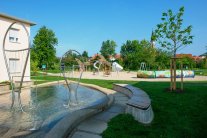 Blick über das Wasserbecken mit Skulpturen zum Spielplatz mit dem Seeräuberschiff.