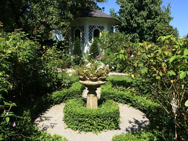 Blick auf runde Formbuchshecke mit Pflanzschale und Pavillon