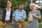 Drei Personen stehen im Garten und lachen