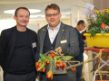 Zwei Besucher der Tagung in der Ausstellung vor bepflanzten Blumenkästen.