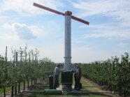 Mitarbeitern stehen auf den Obstanlagen an der Windmaschine unter blauem Himmel mit Wolken