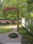 Ein Garten mit Rondell, Kiesfläche, oavlem Pflanzbeet und am Rand eine Pflanzfläche mit einem Baum.