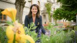 Ministerin Kaniber hinter Blütenpflanzen, im Hintergrund das Ministeriumsgebäude
