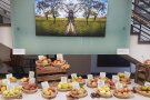 Weißer Tisch auf dem braune Körbchen mit Äpfeln und Sortenschilder sehen. Im Hintergrund ist ein gespiegeltes Bild eines Streuobstbaumes aufgehängt. 
