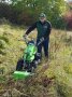 Ein Mitarbeiter eines Geräteherstellers führt ein einachsiges Messerbalken-Mähgerät vor. Er hat bereits einen breiten Streifen in eine dichte Wiese gemäht.