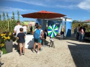 Besucher unter einem roten Sonnenschirm neben Glücksrad und Ausstellungspavillon