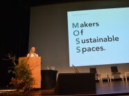 Kelai Diebel steht am Rednerpult. Im Hintergrund an der Leinwand steht Makers Of Sustainable Spaces.