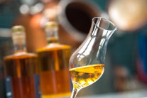 Ein volles Whisky-Glas vor zwei Whisky-Flaschen und der Destille