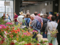 Besucher im Gewächshaus vor einem Tisch mit blühenden Plfanzen.