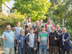 Gruppenbild der Auszubildenden mit Dr. Hermann Kolesch und Albert Cicero an einem Treppenaufgang umgeben von Blumen und Bäumen