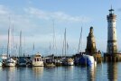 Hafen mit Segelbooten, Einfahrt flankiert von steinernem Löwen und Leuchtturm