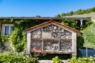 Ein großes Insektenhotel mit vielseitigem Inventar steht vor einer Weinbergshütte