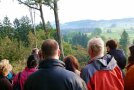 Personengruppe blickt über herbstliche Hecken in eine hügelige Landschaft