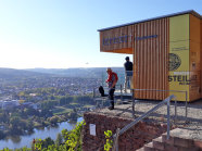 Besucher auf dem Glasbalkon blicken über die Landschhaft und den Main