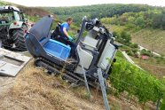 Eine blaue Weinbergsraupe mit aufgebauter Vollerntereinrichtung fährt in eine Rebzeile ein, gehalten von einem starken Drahtseil