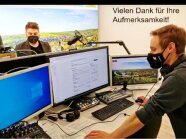 Ein Mann mit Headset vor drei Bildschirmen, dahinter Großes Mikrofon und Referent