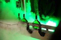 Grüne Glasflaschen von hinten beleuchtet und von Nebel umhüllt auf einem Metallsteg  