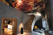 Blick in eine Vinothek, eine Treppe führt hinauf,die Decke mit Rosenmotiv geschmückt, Ein Sitzplatz vor einem großen Fenster und im Hintergrund die Bar für den Weinverkauf
