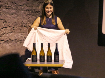 Die Fränkische Weinkönigin Carolin Meyer hebt ein Tuch an unter dem vier Weinflaschen stehen.
